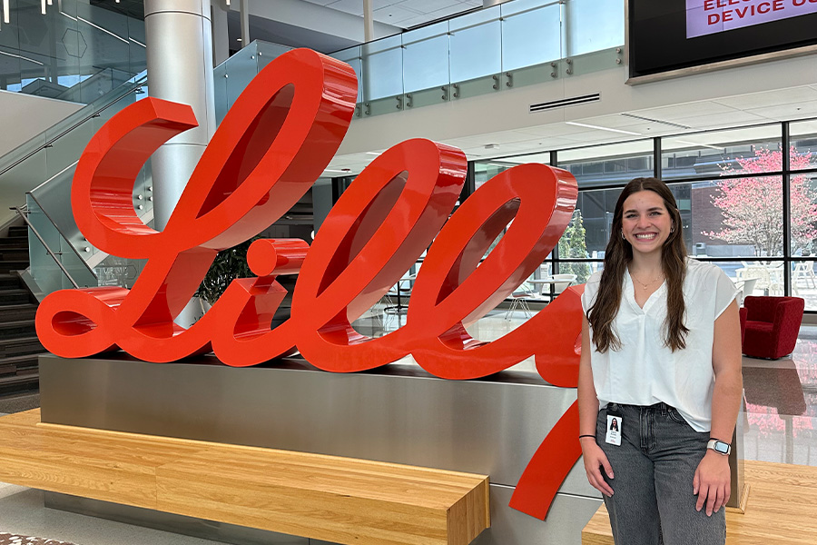 Student with dark hair smiling in fron t of Lilly sign